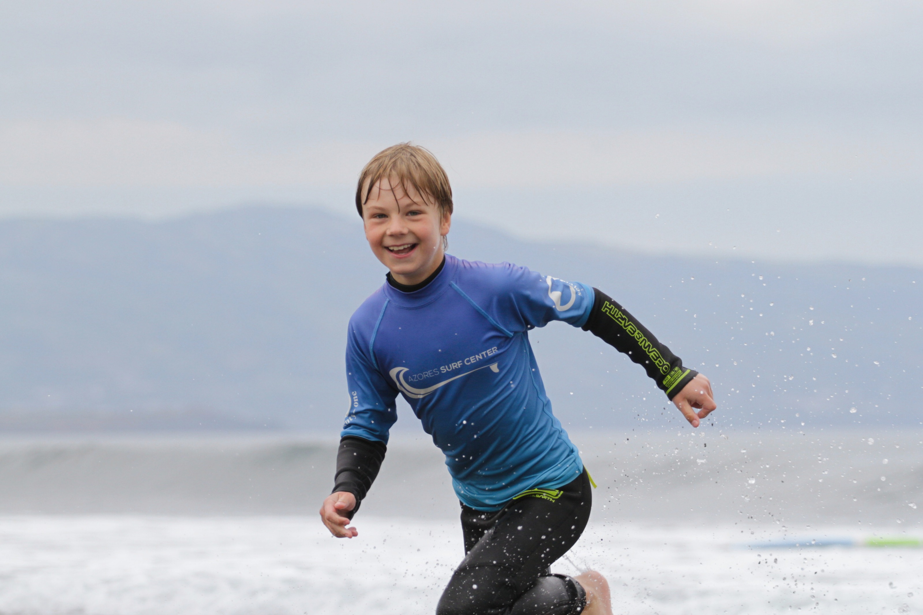 Niño con licra azul corriendo y sonriendo junto a la laguna