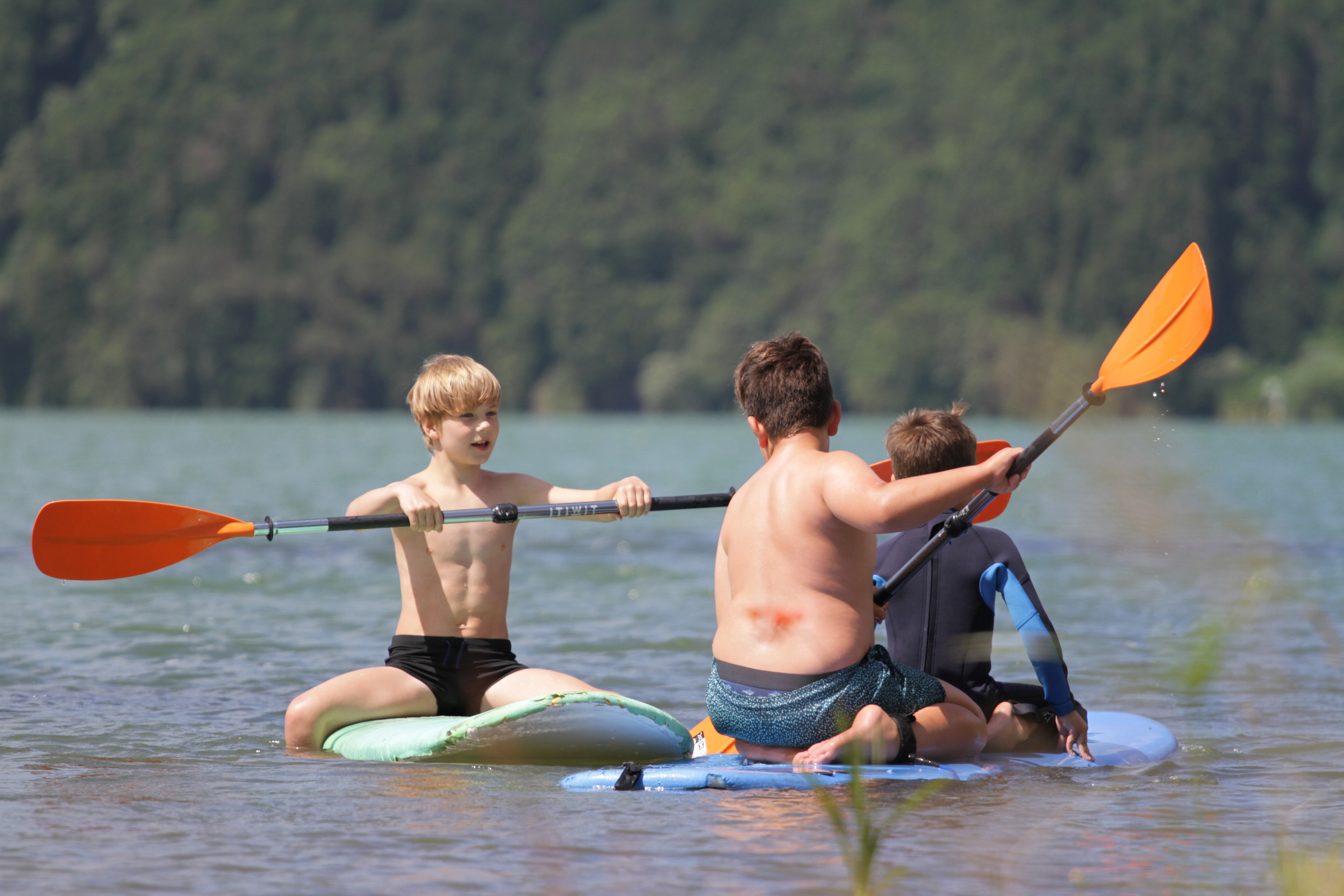 Tres niños con remos sobre tablas de paddle en la laguna