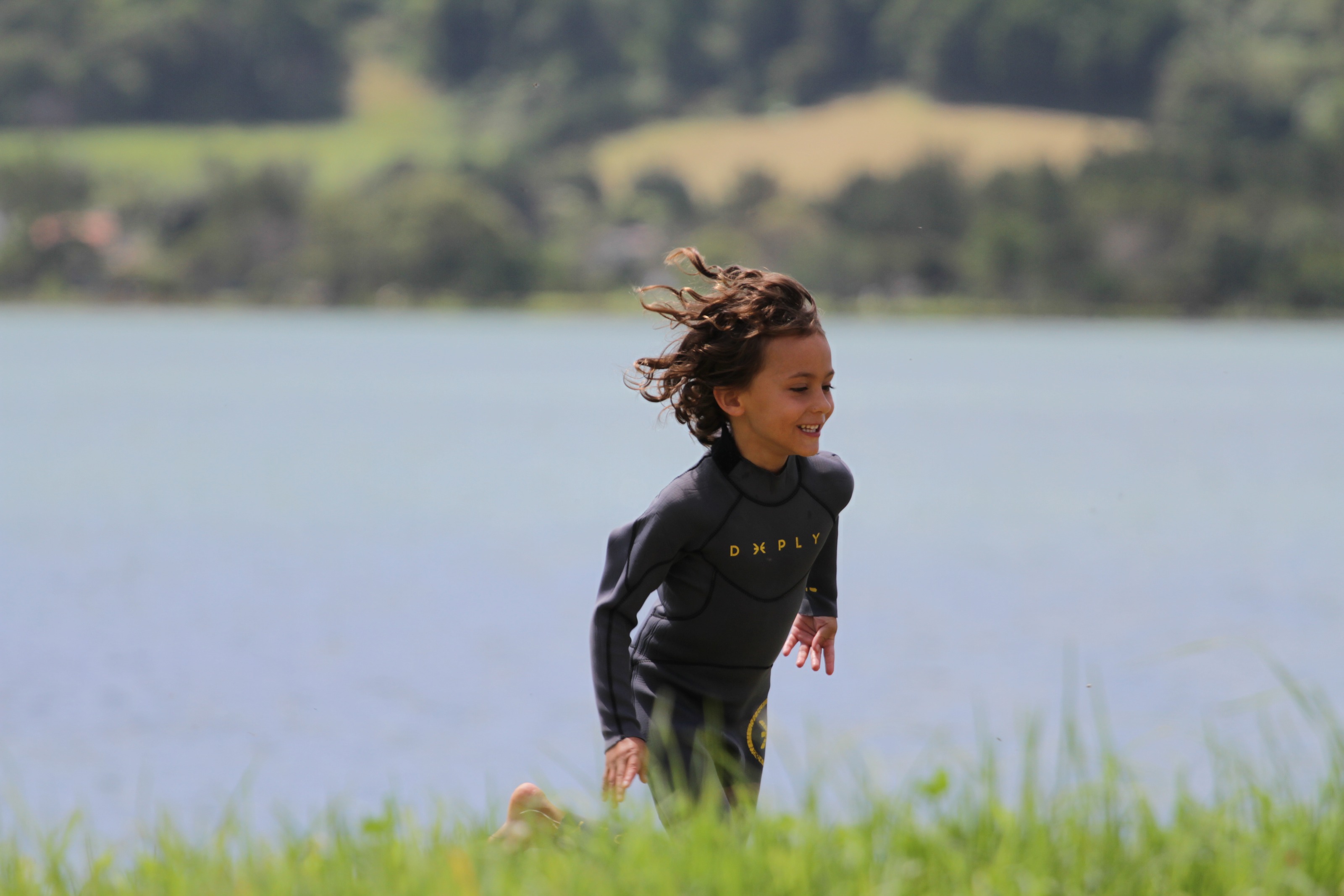 Niño con neopreno corriendo por la hierba junto a la laguna