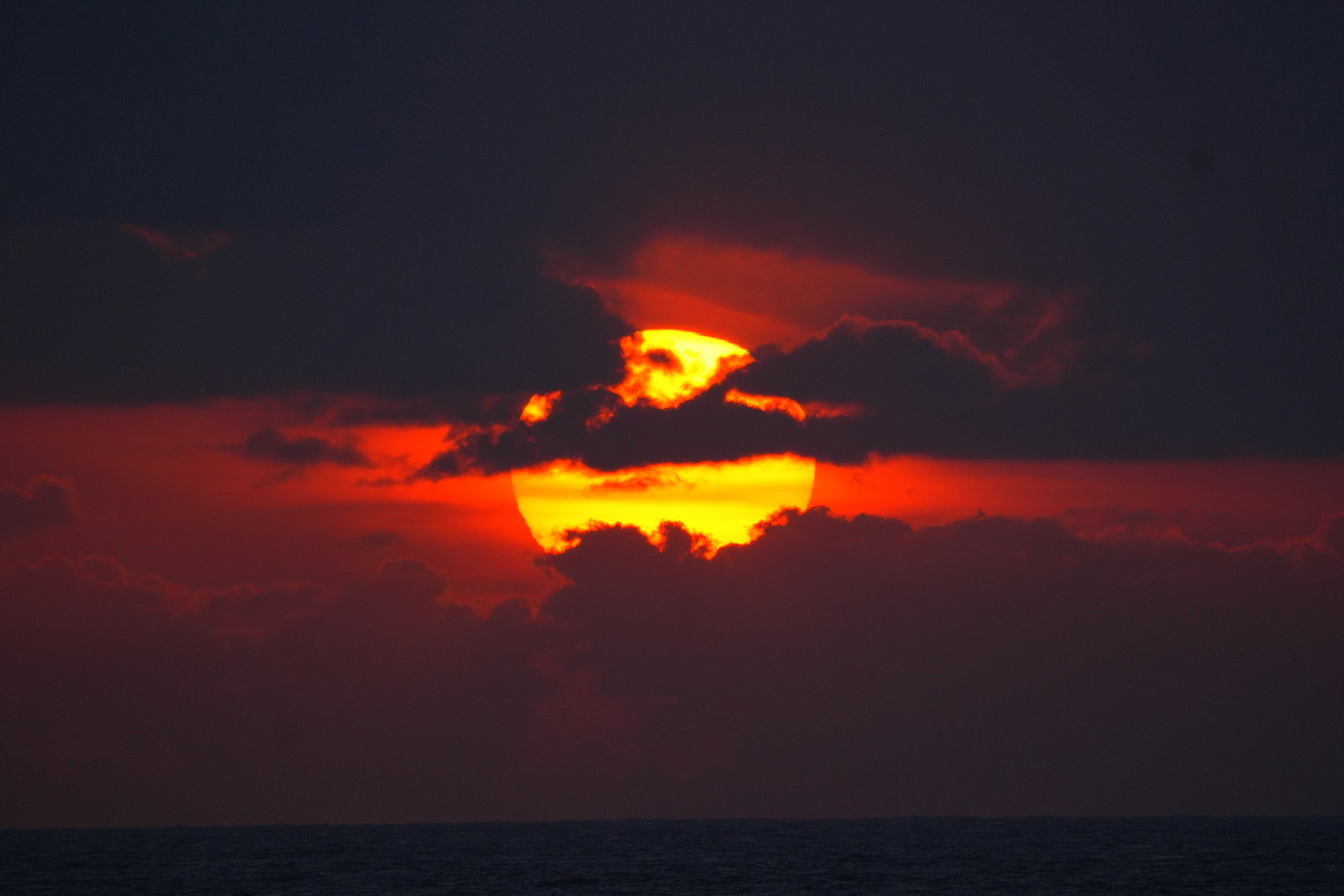 A red sun setting through the clouds over the sea